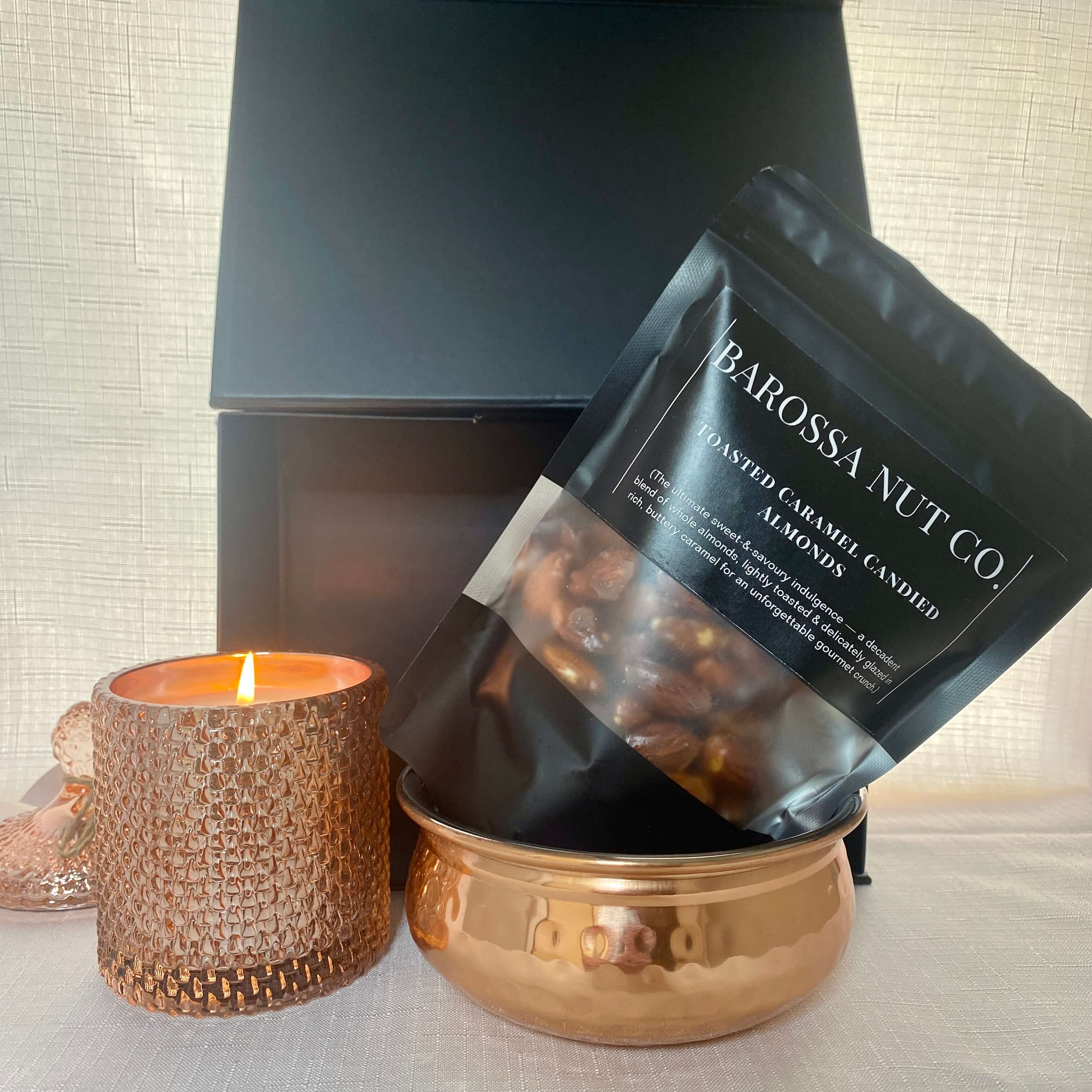 Barossa Nut Co. roasted caramel candied almonds packaging with a lit candle and decorative bowl.