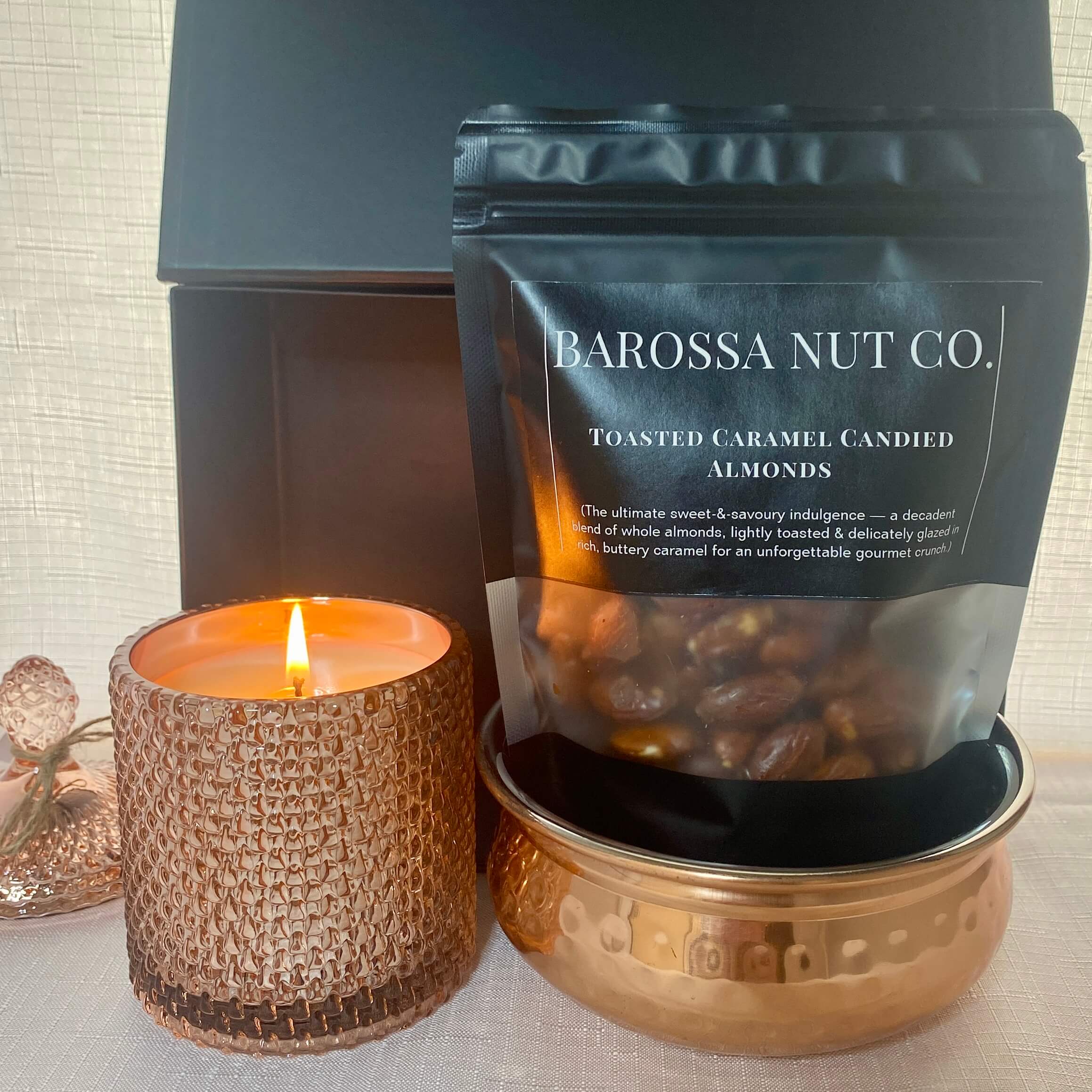 Barossa Nut Co. toasted caramel candied almonds packaging with a lit candle on a textured surface