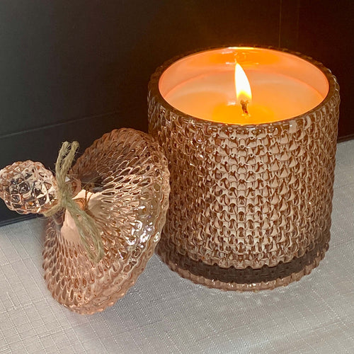 Decorative candle in a textured holder with a lit flame on a neutral background