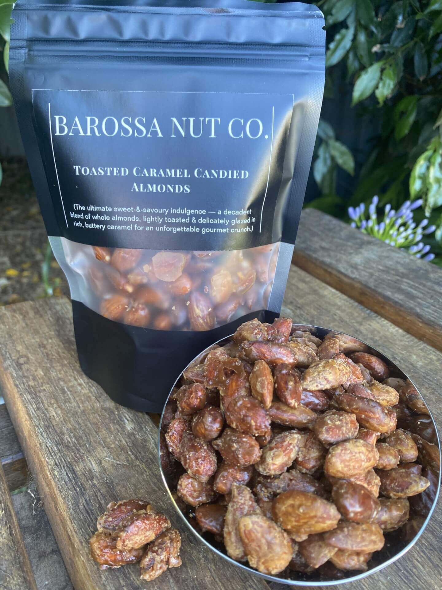 Barossa Nut Co. toasted caramel candied almonds in a scoop and packaging on a wooden surface.