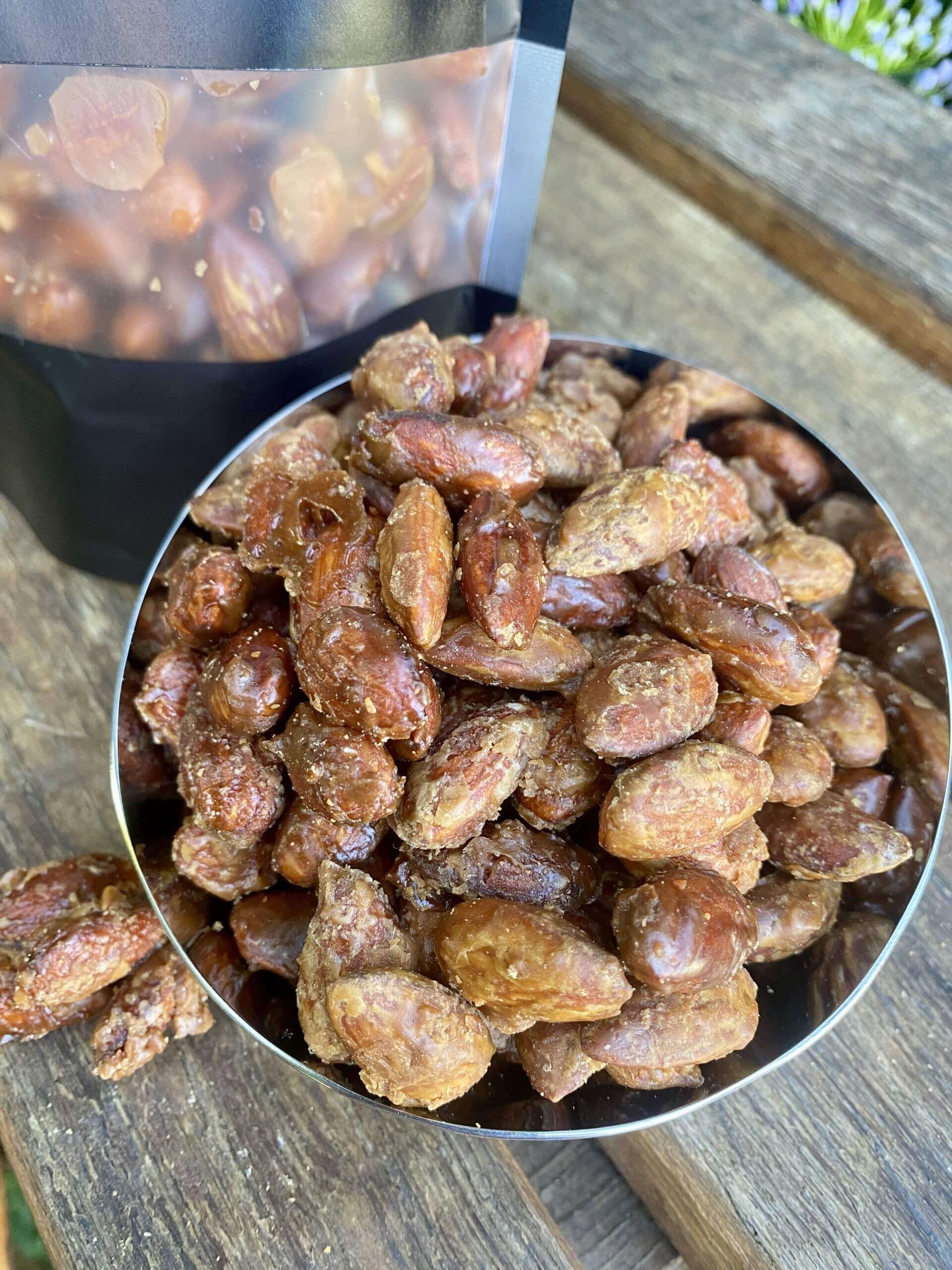 Metal scoop filled with roasted almonds on a wooden surface